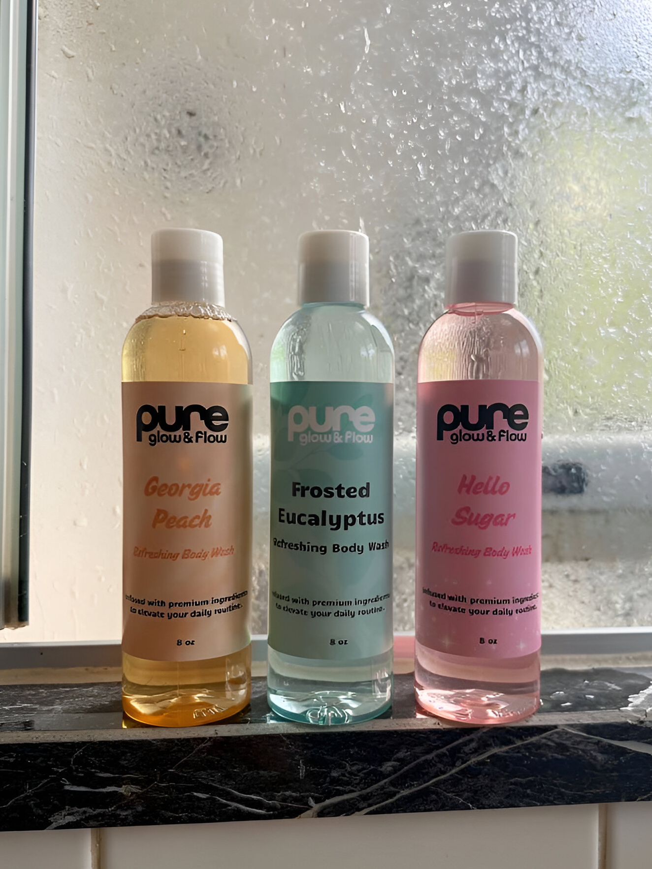Three bottles of 'pure glow & flow' body wash on a windowsill with a blurred background.